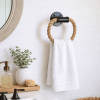 A circular black rope towel holder with a natural thick rope attached on a wall next to a sink with white towel