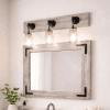 light whitewash wood frame mirror sitting above a white vanity with 3 jars light on top