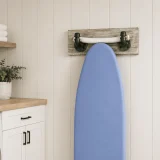 Light Whitewash wood ironing board wall hanger with Dark Nickel pipe hooks holding the T-shaped leg of a folded ironing board