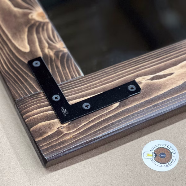 Close-up of Coffee-stained pine mirror frame showing natural wood grain and a dark nickel metal corner bracket.